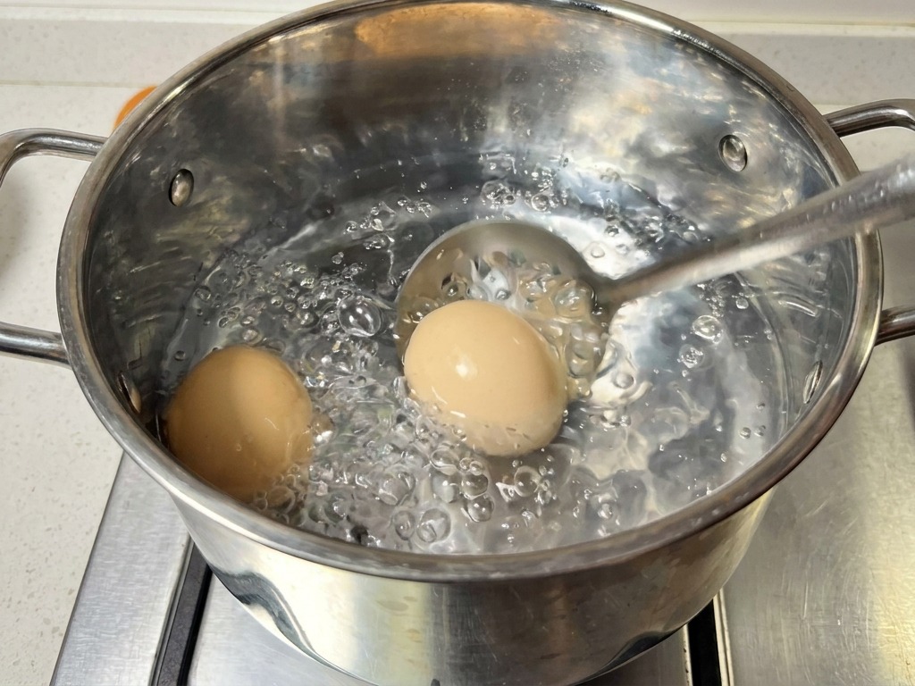 Una espumadera de acero inoxidable sacando dos huevos de una olla con agua hirviendo.