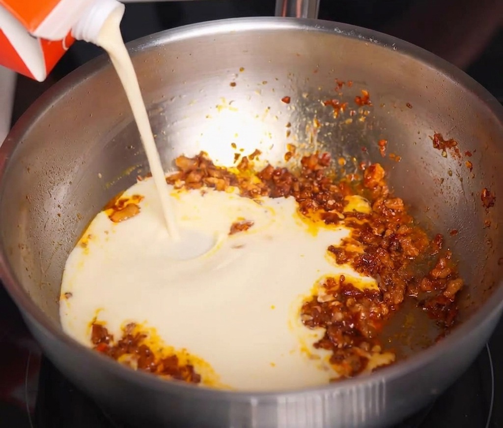 Leche de soja blanca vertiéndose desde un brik sobre la carne sazonada.