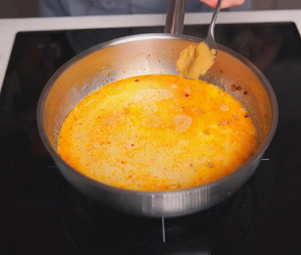 Una cucharada de miso de color marrón claro añadiéndose al caldo cremoso.