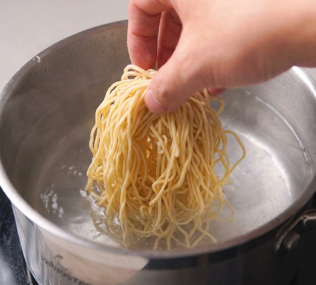 Una olla de acero con agua al fuego con pequeñas burbujas formándose en el fondo.