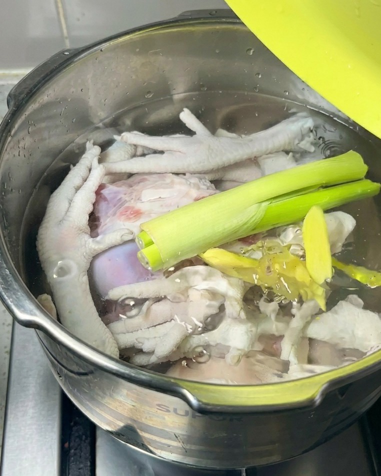 Cebolletas verdes frescas y rodajas de jengibre reposando sobre la carne cruda y el agua dentro de una olla.