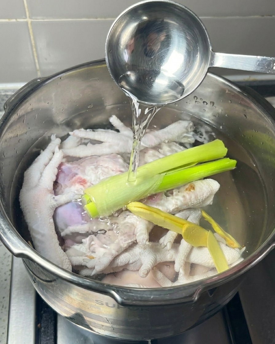 Olla a presión con patas de pollo, jengibre y cebolleta mientras se vierte vino blanco desde un cazo de metal.