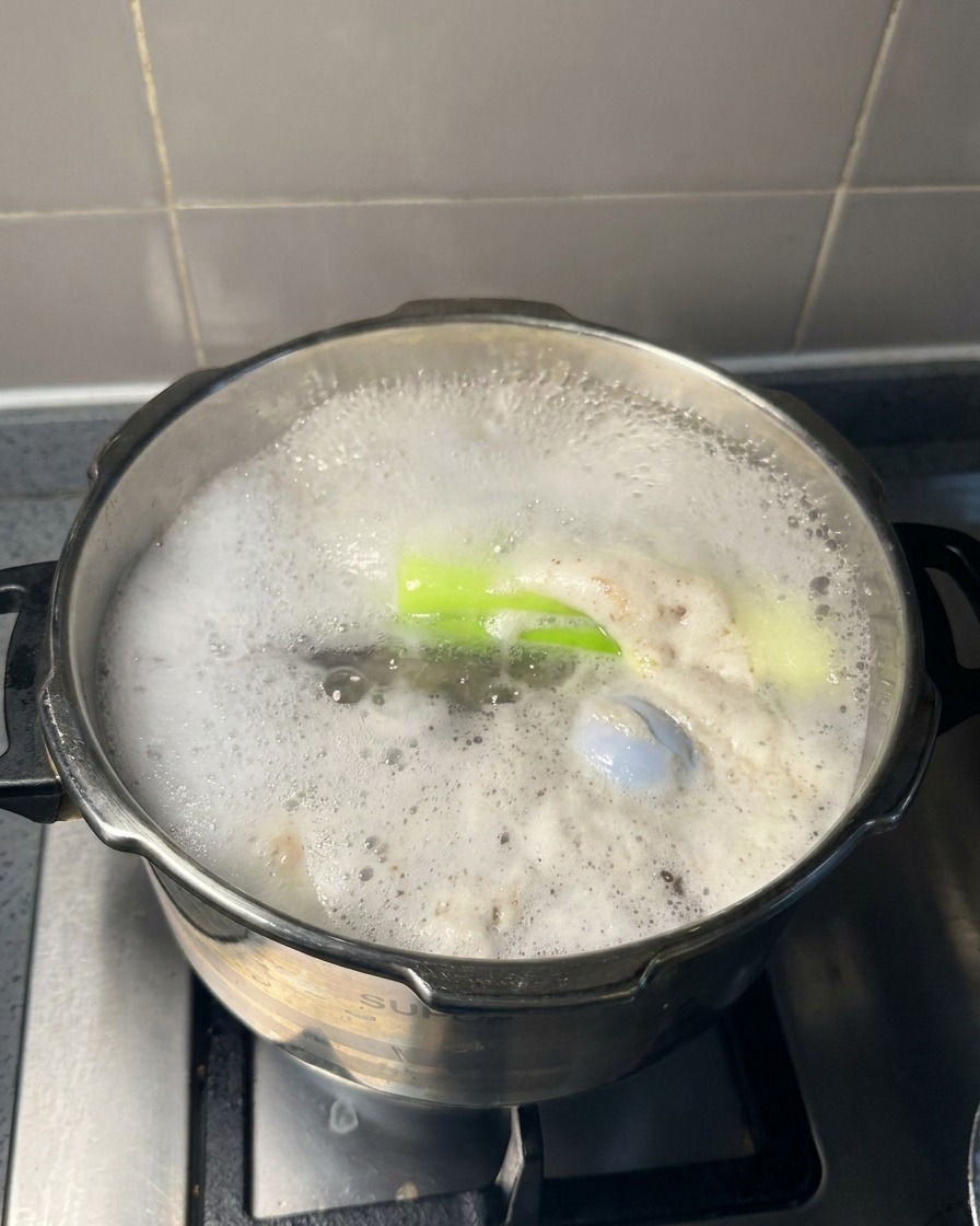 Cuchara de metal grande retirando espuma gris de la superficie de un caldo de carne hirviendo.