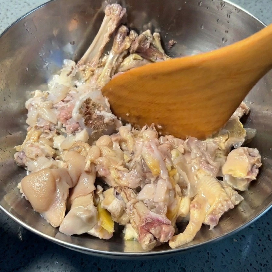 Espátula de madera presionando manita de cerdo y patas de pollo cocidas en un bol para separar la carne y la piel de los huesos.