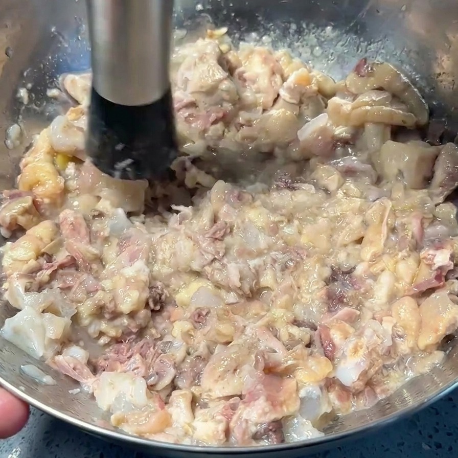 Machacador de metal triturando carne de cerdo y pollo cocida hasta formar una pasta espesa en un bol.