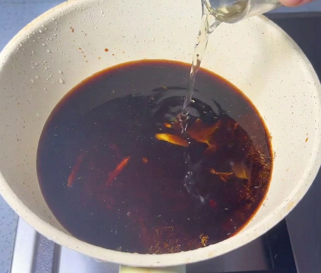 Líquido transparente vertiéndose en una cacerola con salsa oscura y polvo de pescado