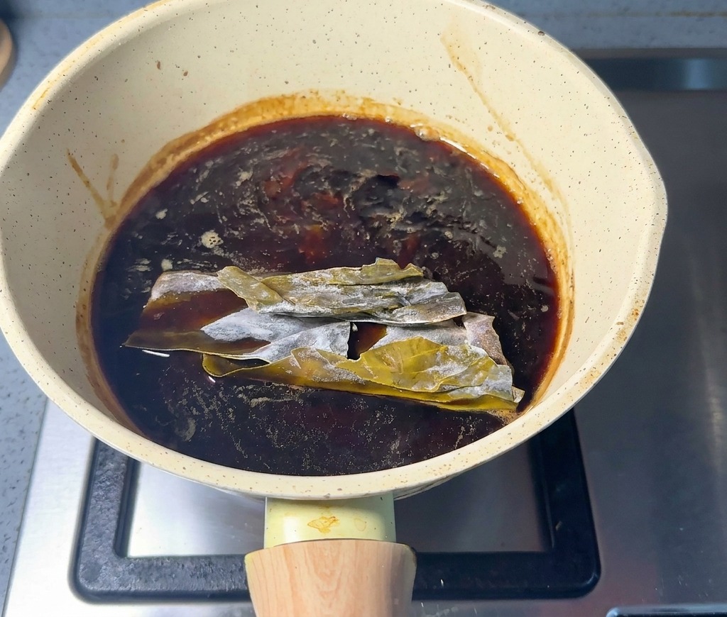 Láminas de kombu seco sumergidas en la salsa oscura dentro de una cacerola