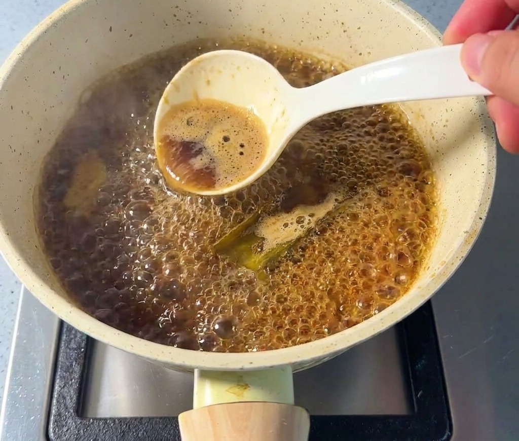 Una mano usando una cuchara blanca para quitar la espuma de una salsa burbujeante