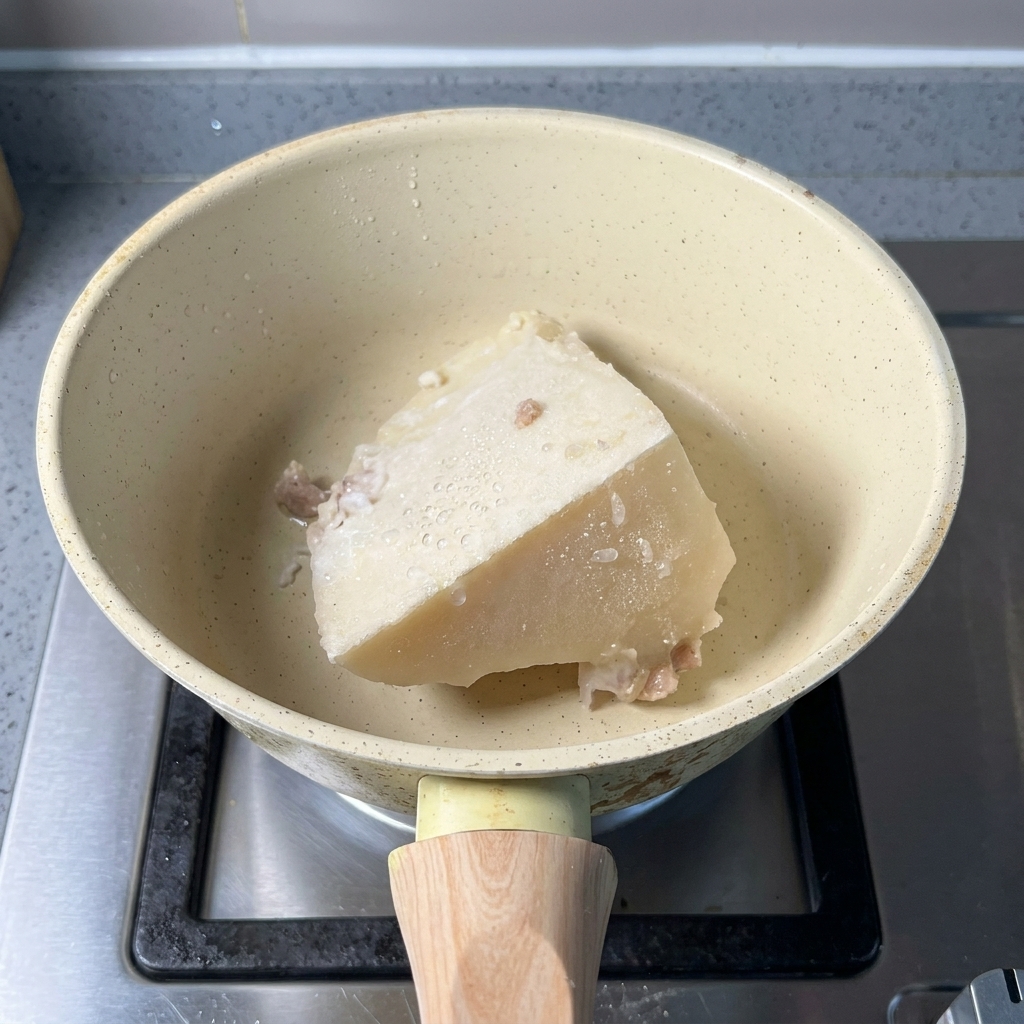 Un bloque de caldo de cerdo congelado y una cucharada de polvo de pescado en una cacerola