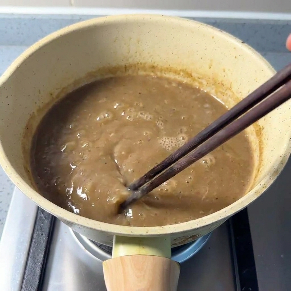 Removiendo con palillos un caldo espeso de cerdo mezclado con polvo de marisco
