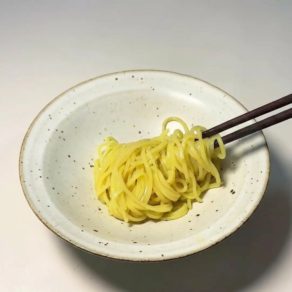 Palillos de madera colocando un nido de fideos amarillos en un bol de cerámica moteado