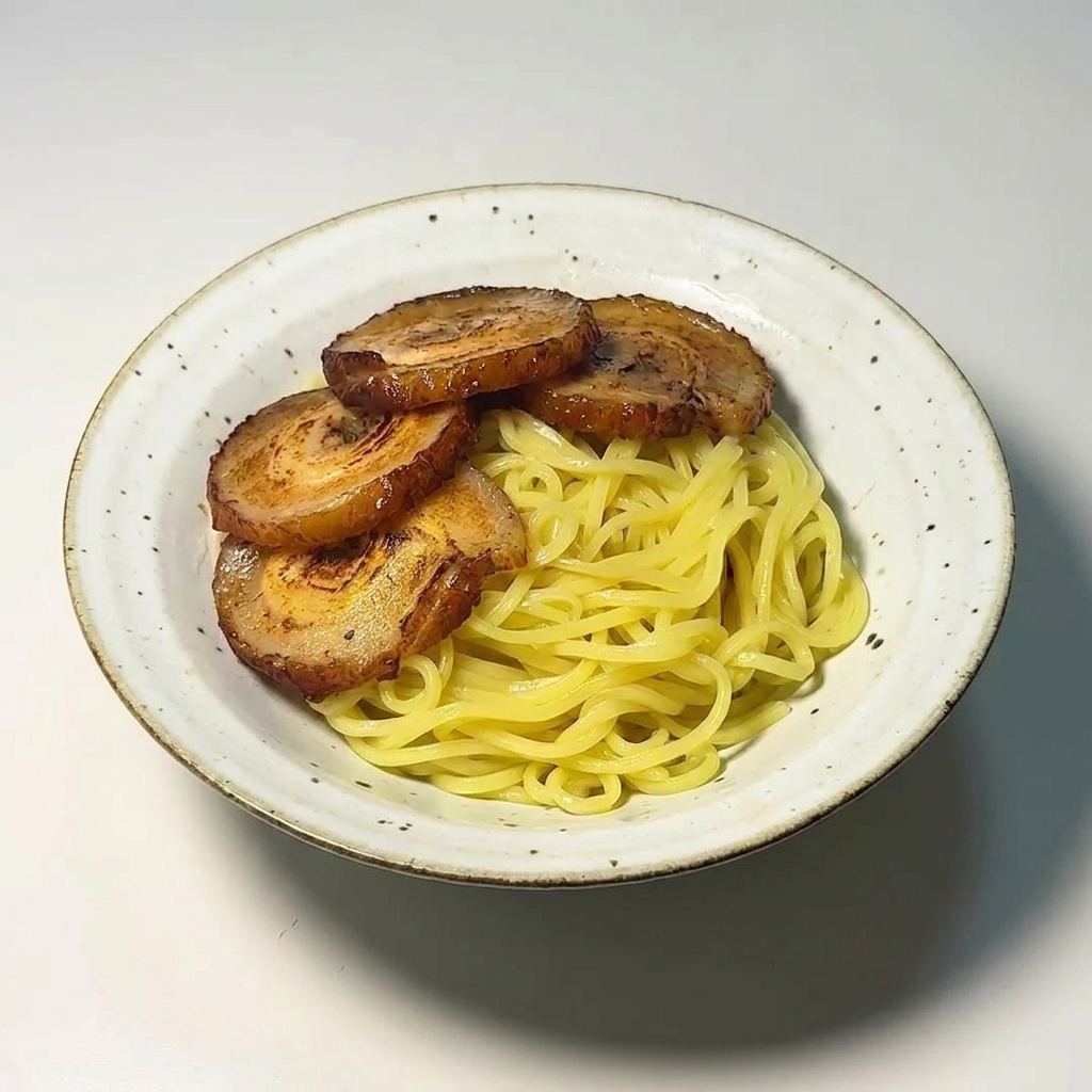 Cuatro rebanadas de cerdo chashu dorado sobre una cama de fideos amarillos