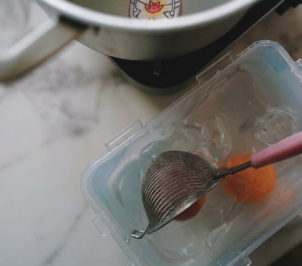 Un colador levantando un huevo cocido de una olla y sumergiéndolo en un recipiente con agua y hielos.