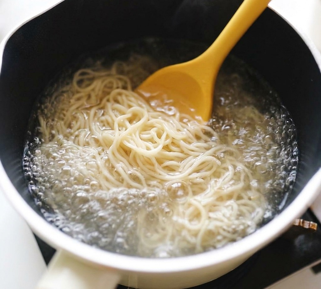 Fideos ramen rizados siendo removidos con una cuchara en una olla con agua hirviendo.