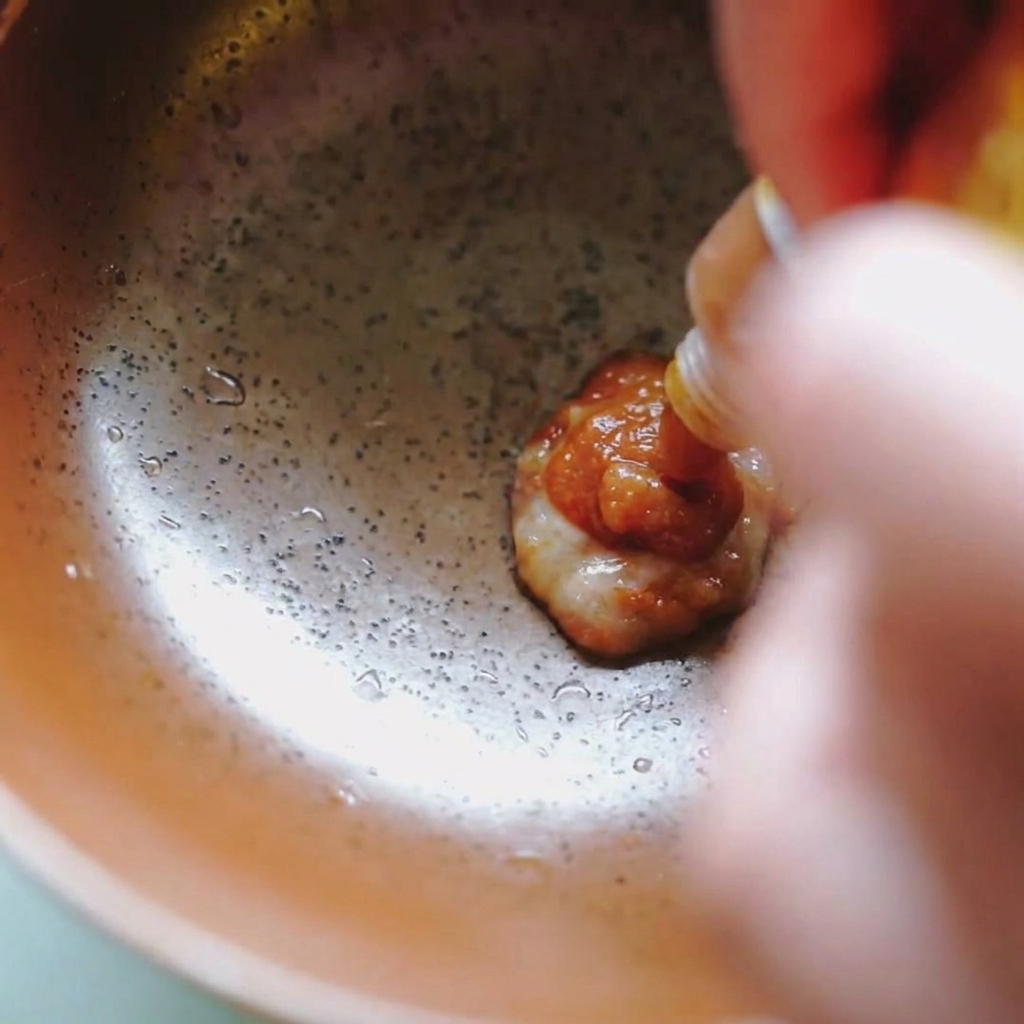 Pasta de miso espesa y marrón saliendo de un sobre hacia un bol de cerámica.