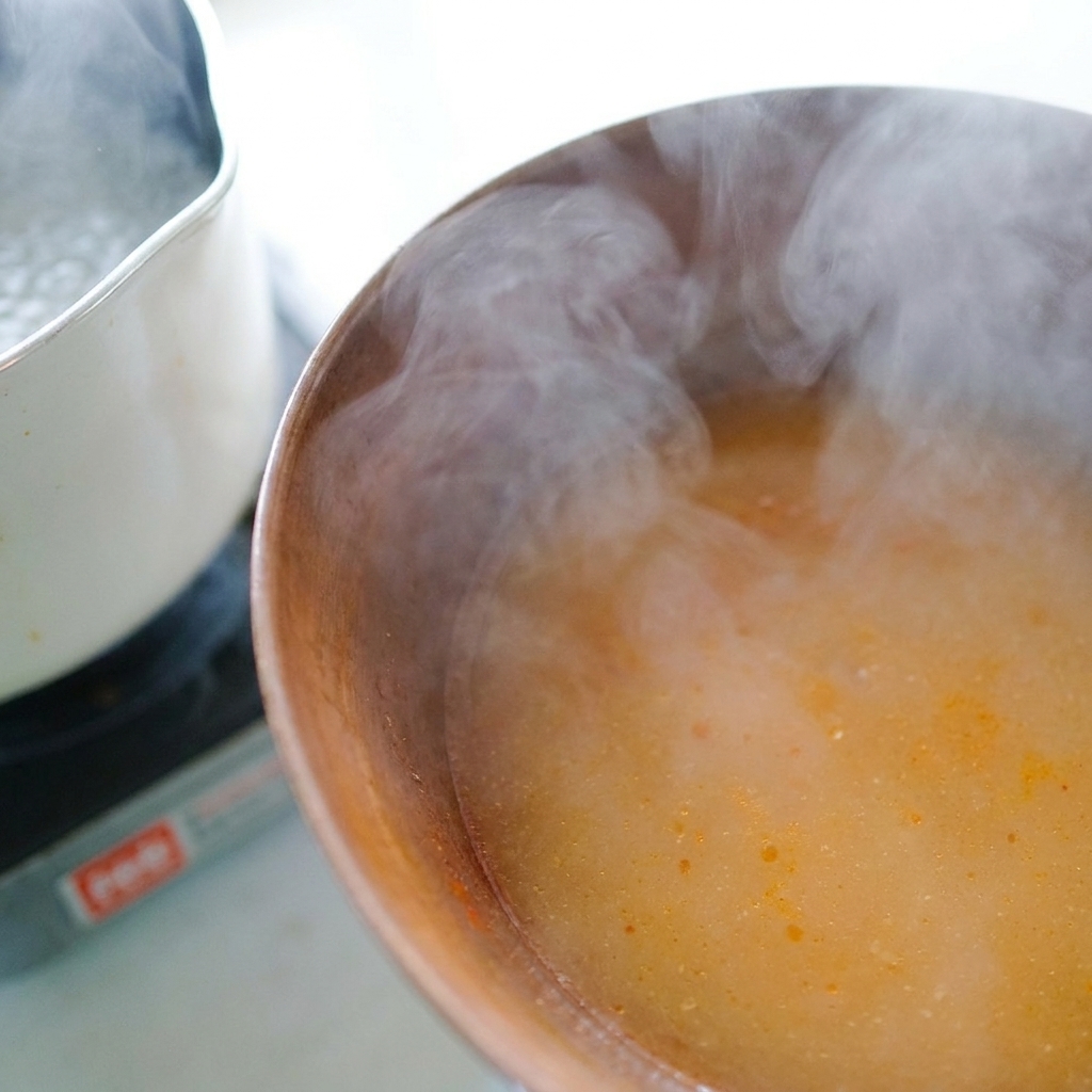 Agua caliente de la cocción de los fideos siendo vertida con un cucharón en el bol con la pasta de miso.