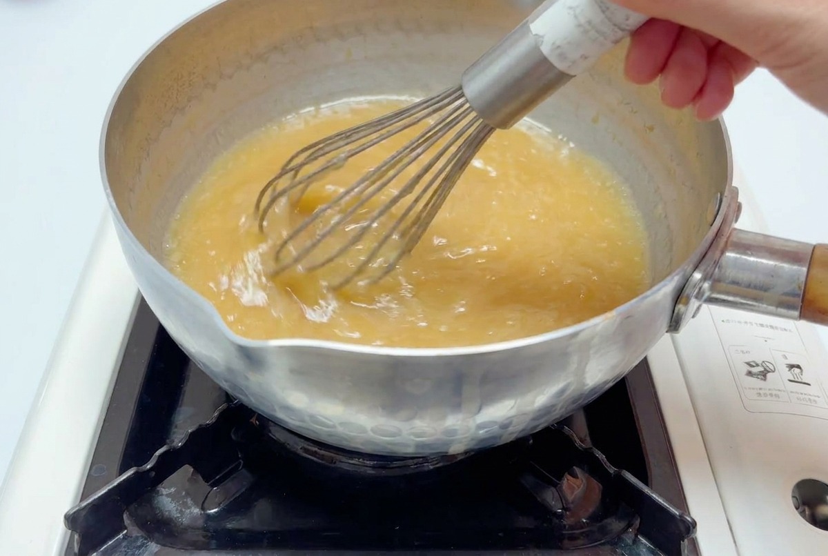 Batidor de varillas mezclando el caldo de miso en una olla hasta que esté totalmente integrado.