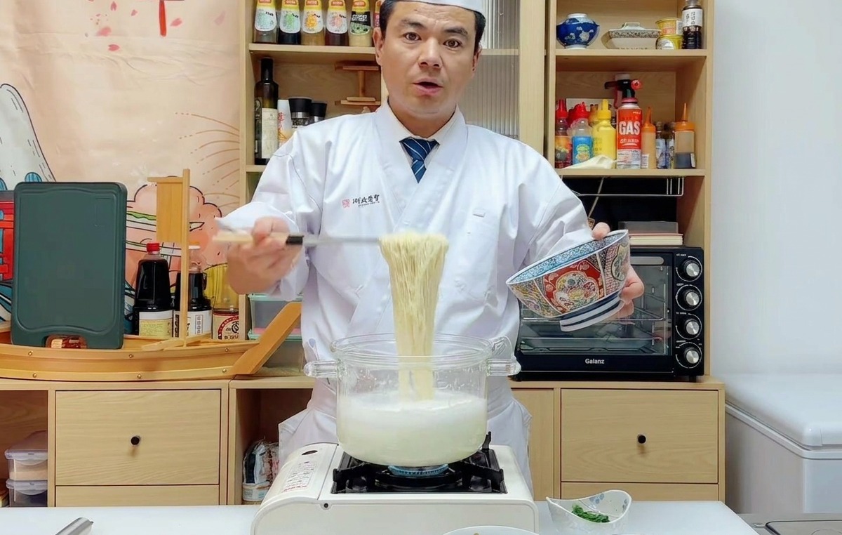 Cocinero usando un colador para pasar los fideos ramen cocidos a un bol azul decorado.