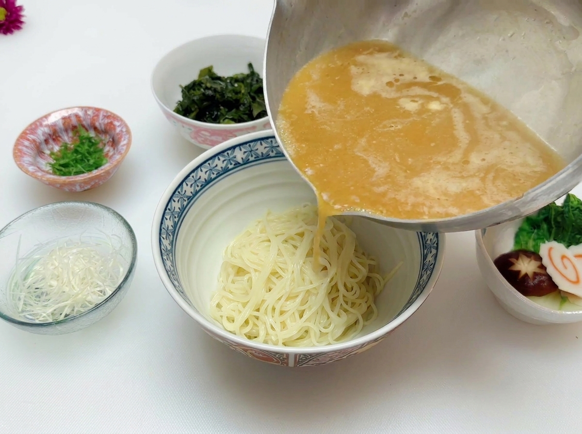 Caldo de miso caliente vertiéndose desde la olla sobre los fideos ramen en el bol.