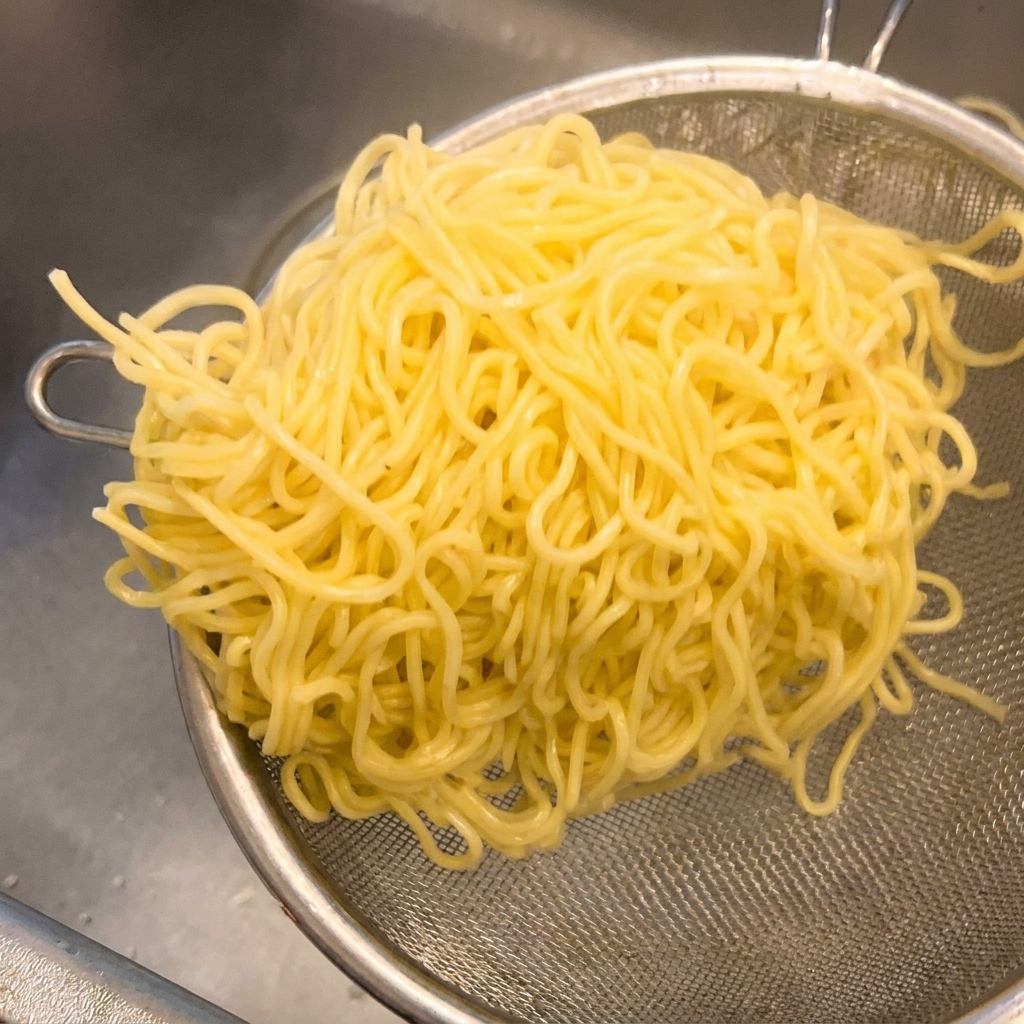 Fideos ramen amarillos cocidos en un colador de malla metálica agitándose para eliminar el exceso de agua.