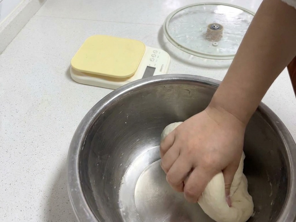 Una mano amasando una bola de masa redonda y suave en un bol de metal para lograr una textura elástica.