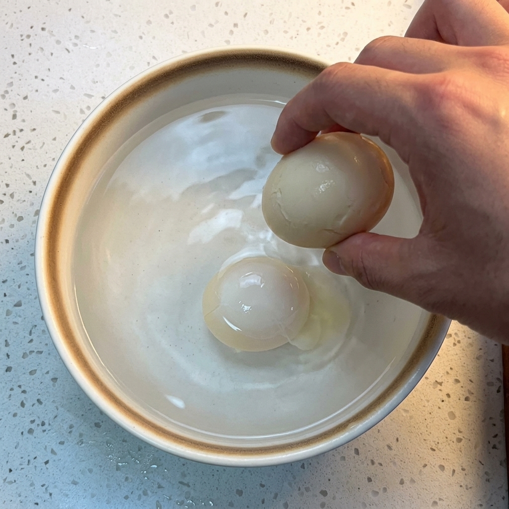 Un huevo cocido sumergiéndose en un cuenco de cerámica blanca con agua y cubitos de hielo.