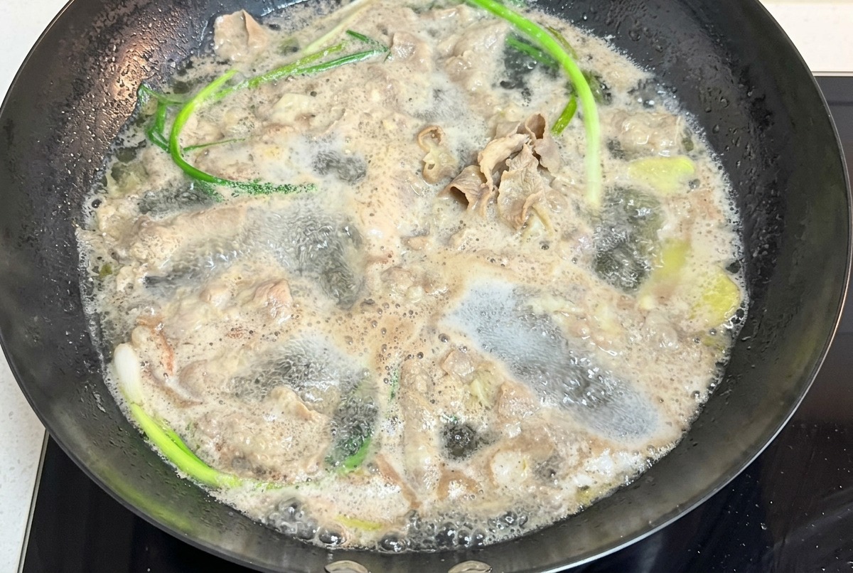 Láminas finas de ternera hirviendo en una olla con agua y tallos de cebolleta.