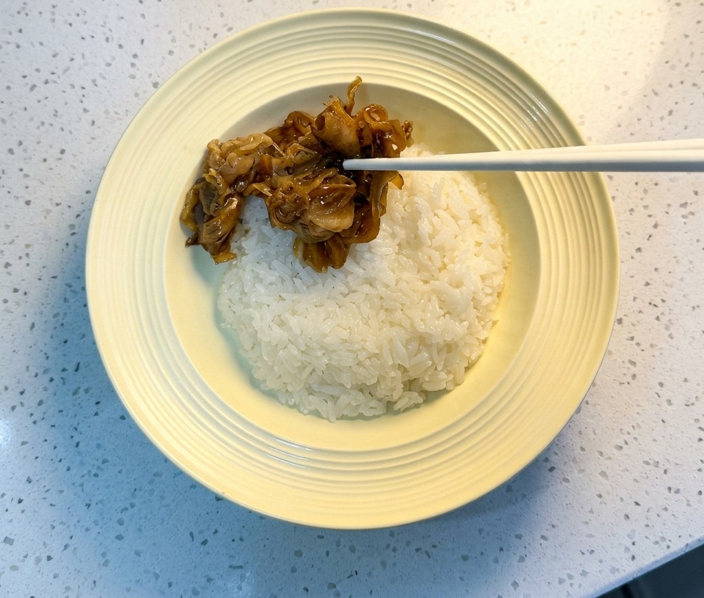 Palillos chinos colocando la ternera glaseada sobre un cuenco de arroz blanco.