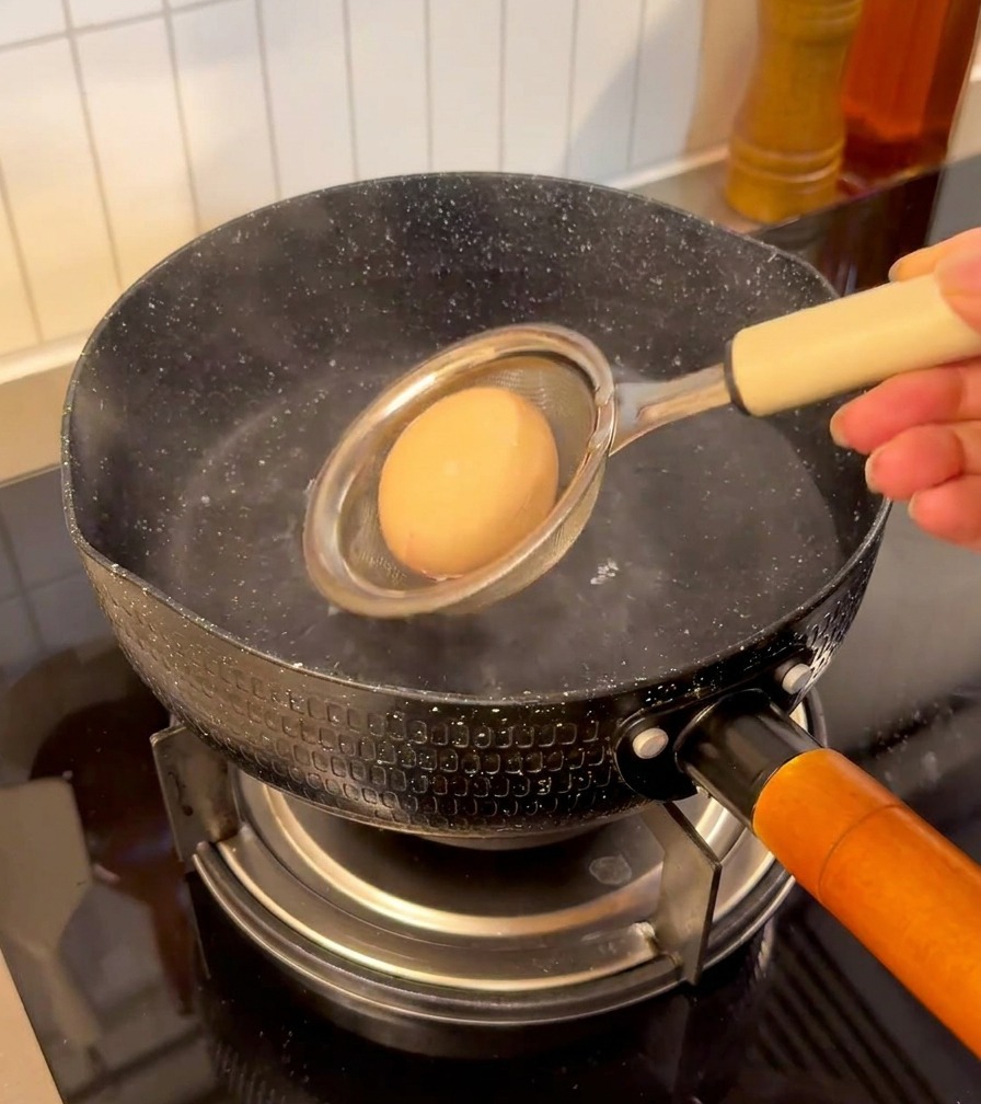Un huevo en un colador de malla sumergiéndose en una olla con agua humeante.