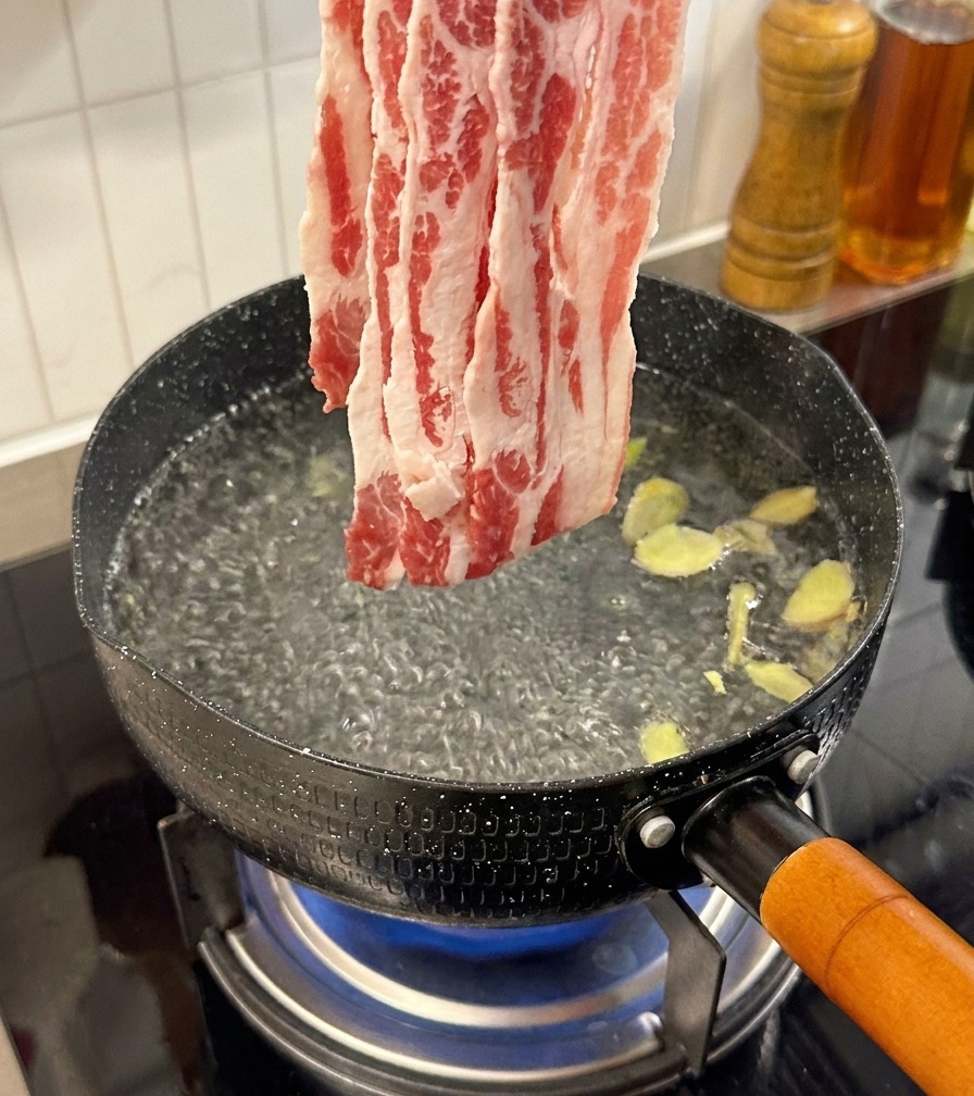 Tiras de ternera cruda añadiéndose a una olla de agua hirviendo con rodajas de jengibre.