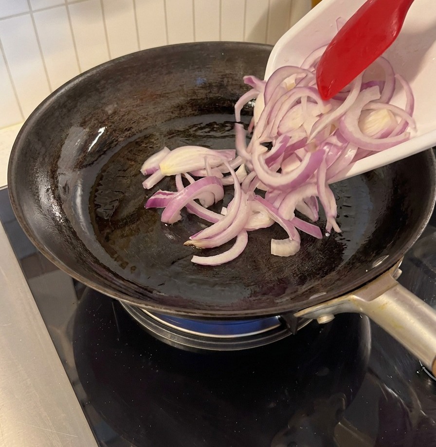 Cebolla morada cortada añadiéndose a una sartén caliente con una espátula de silicona.