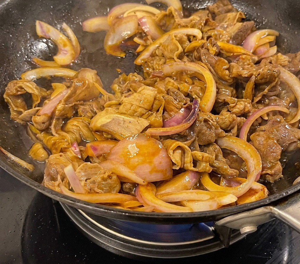 Ternera teriyaki y cebollas hirviendo en una salsa oscura y brillante dentro de un wok.