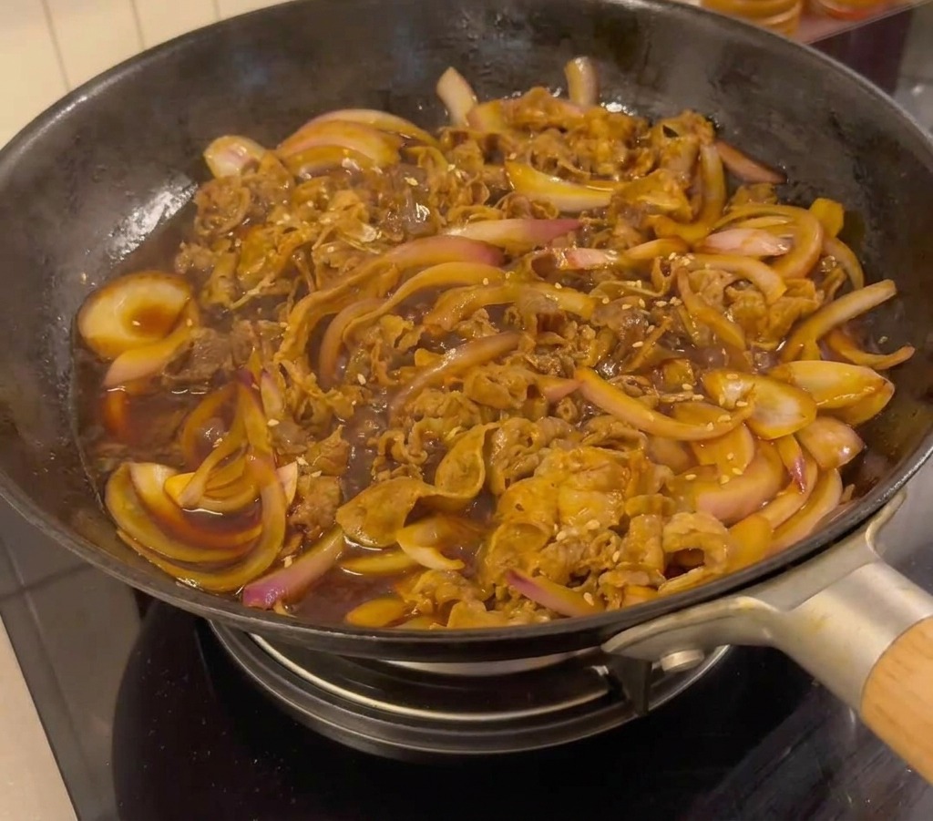 Ternera teriyaki terminada en la sartén decorada con semillas de sésamo y cebollino.