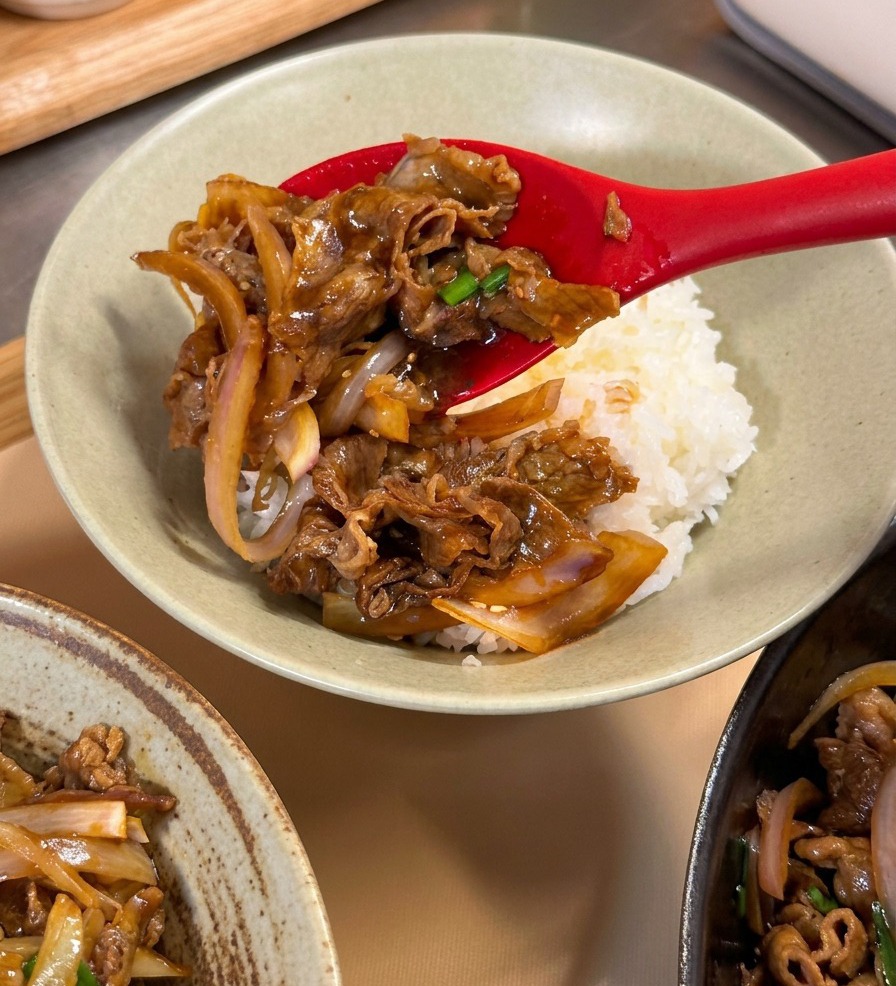 Una cuchara colocando ternera teriyaki sobre una base de arroz blanco en un bol.