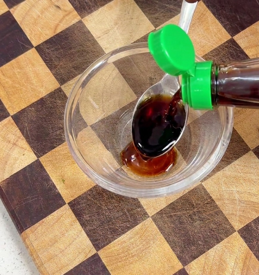 Salsa de soja vertiéndose desde una botella en un bol de cristal con otros condimentos.