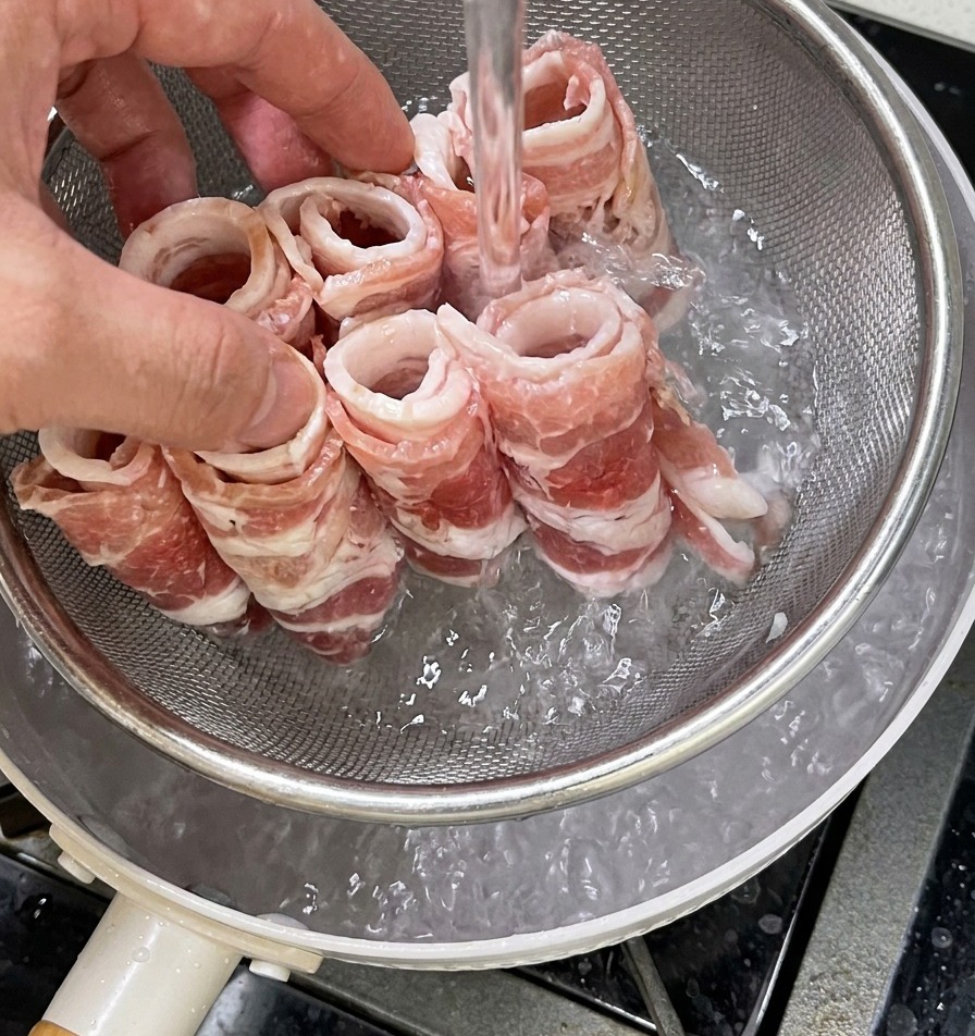 Un colador metálico con láminas de ternera cruda sumergiéndose en una olla de agua hirviendo.
