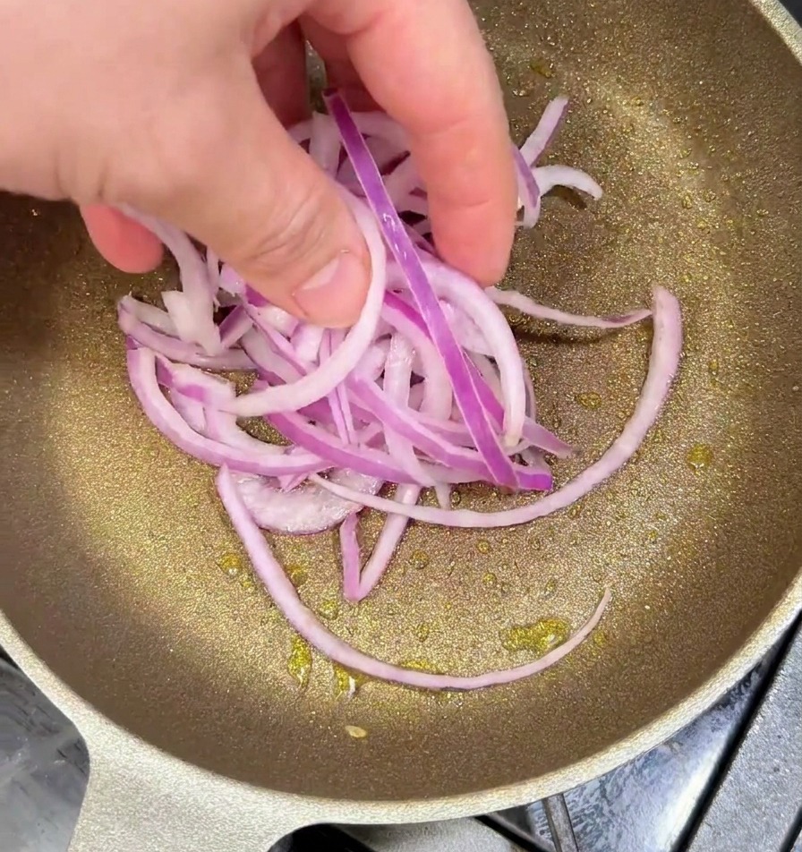 Cebolla morada en rodajas salteándose en una sartén caliente con aceite hasta dorarse.
