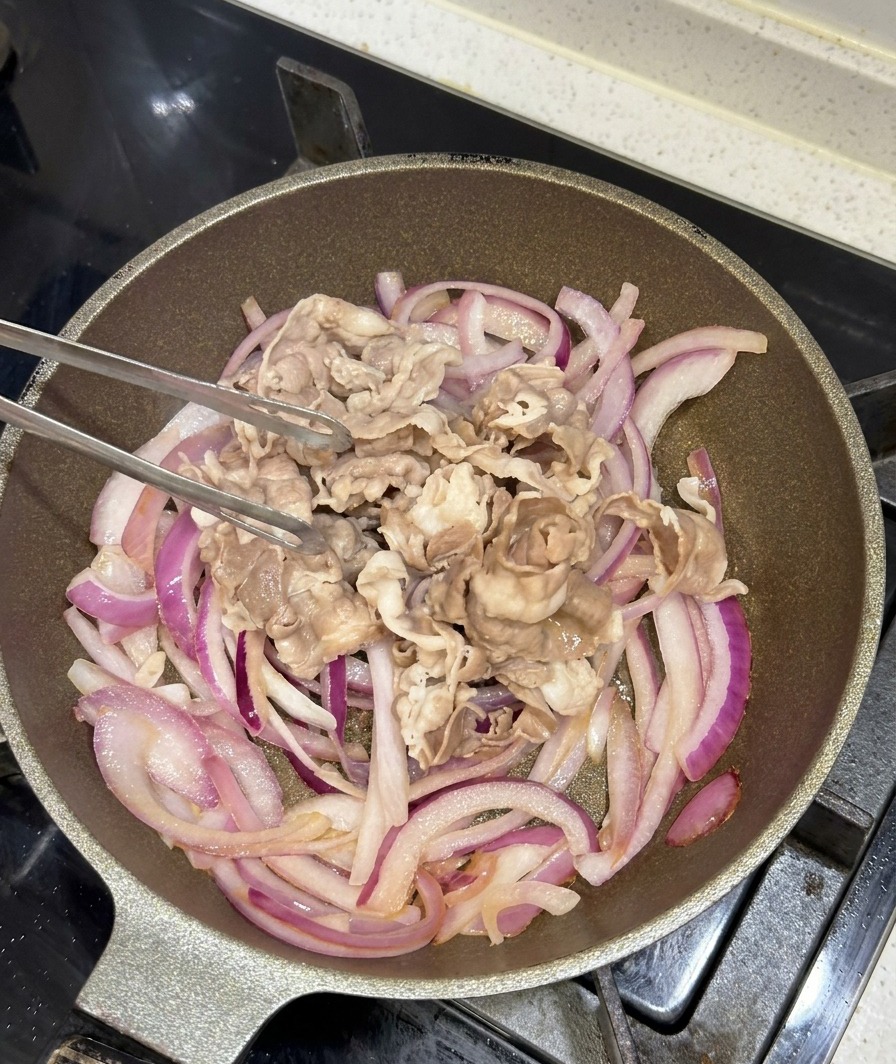 Láminas de ternera blanqueadas añadiéndose a la sartén con la cebolla morada salteada.