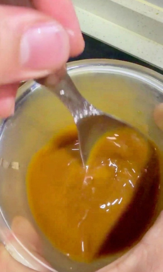 Vertiendo la salsa teriyaki desde un bol a la sartén con la carne y la cebolla.