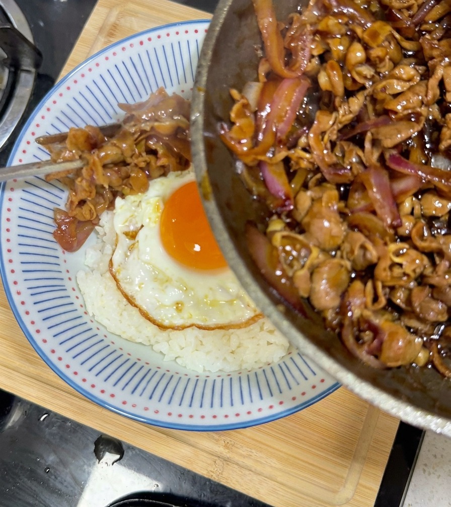Ternera teriyaki glaseada sirviéndose desde la sartén al bol de arroz con huevo.