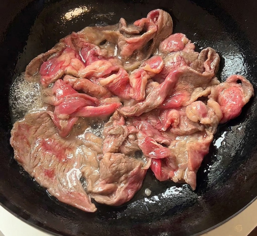 Láminas de ternera doradas y humeantes pasando de una sartén oscura a un plato de cerámica blanca.