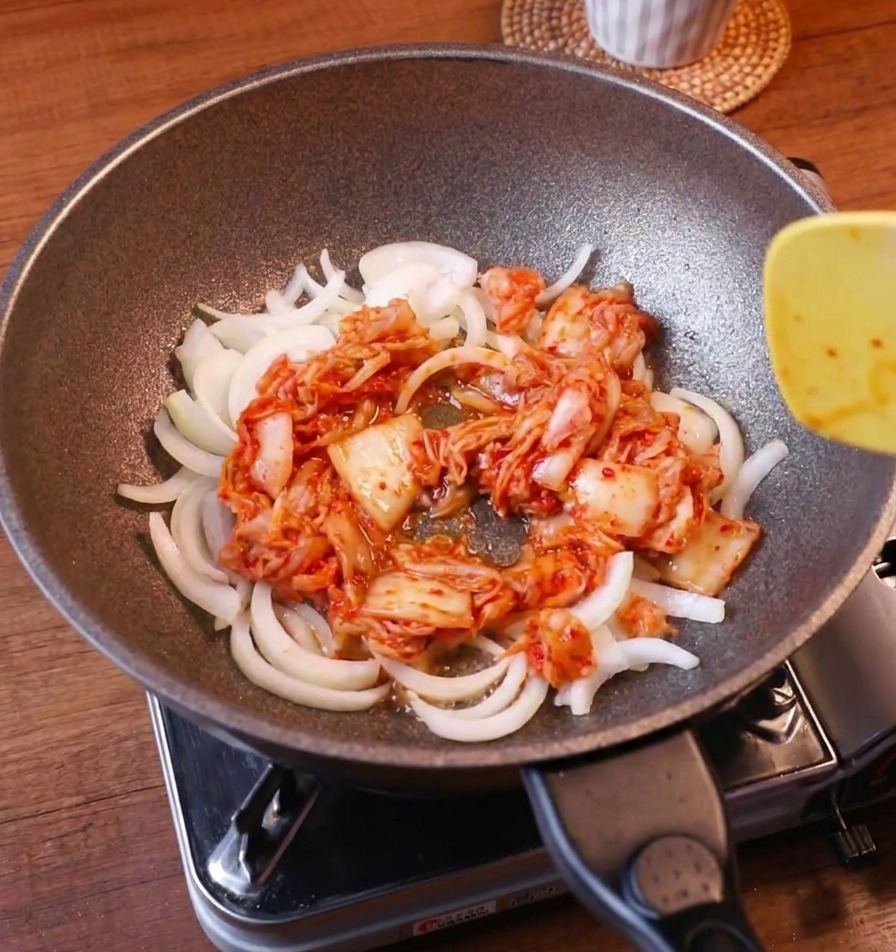 Cebolla blanca y kimchi rojo vibrante salteándose juntos con una espátula amarilla.