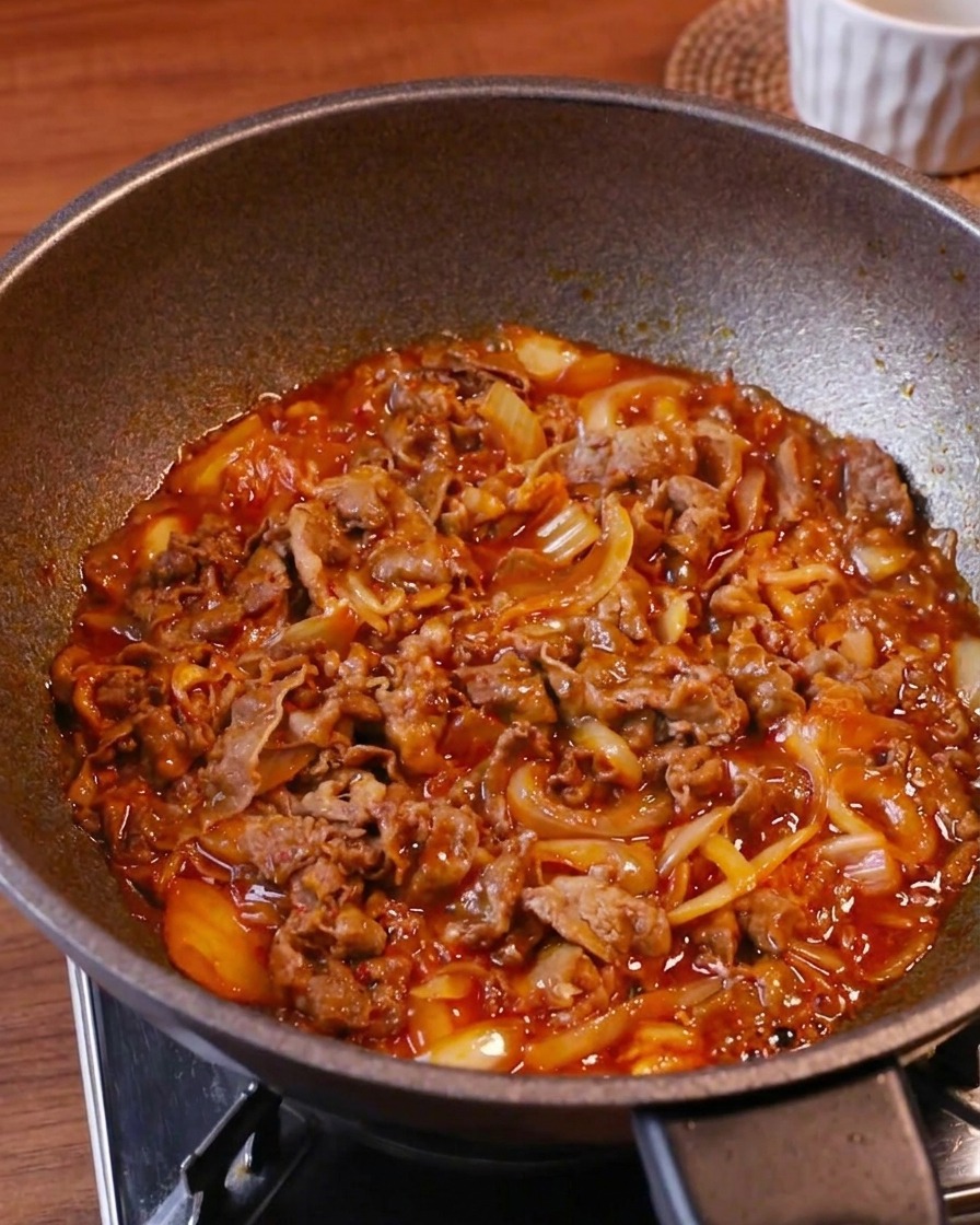 Tiernas láminas de ternera, kimchi y cebolla burbujeando en una salsa roja espesa.