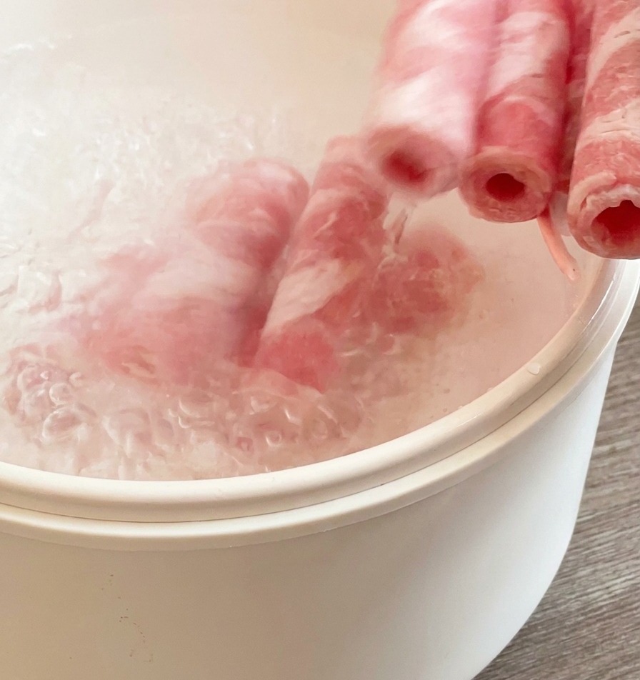 Láminas de ternera congelada sumergiéndose en una olla blanca con agua hirviendo.