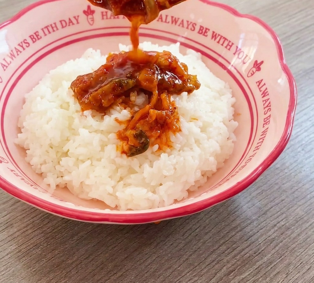Mezcla de ternera y kimchi vertiéndose con una cuchara sobre una montaña de arroz blanco.