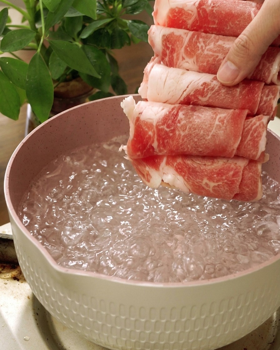 Láminas de ternera cruda introduciéndose en una olla con agua hirviendo.