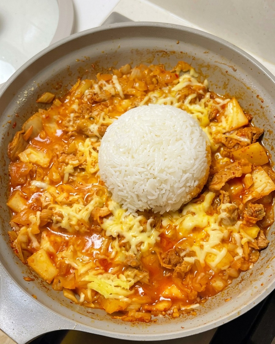 Una montaña de arroz blanco en el centro de la sartén, rodeada de queso fundido y la base de carne y kimchi.