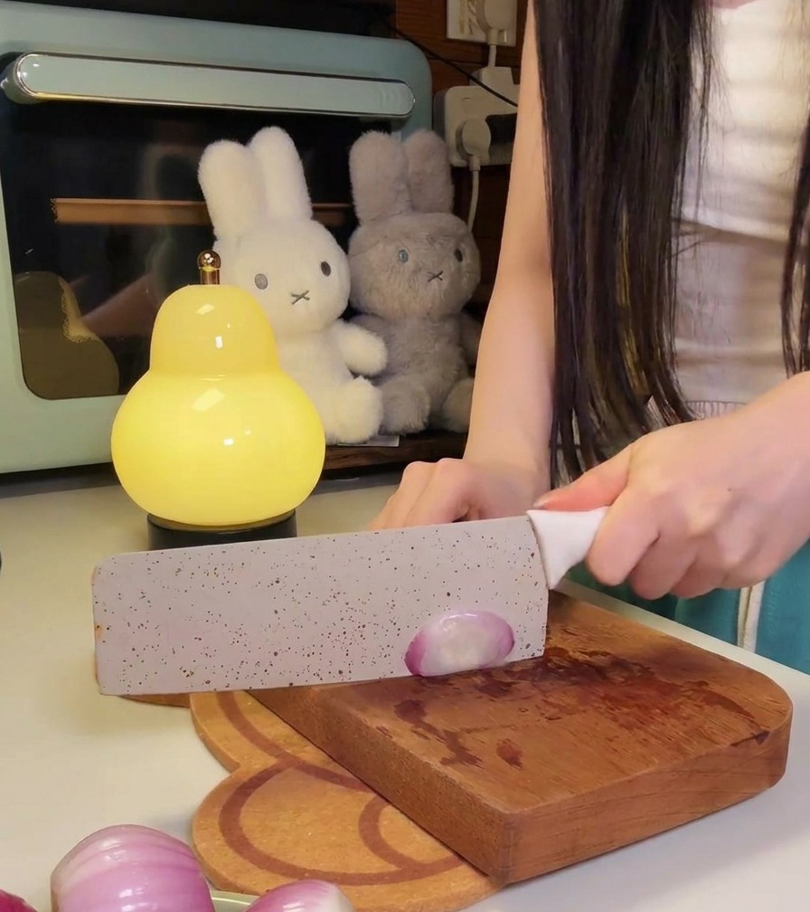Una persona usando un cuchillo de cocina grande para cortar finamente cebollas rojas pequeñas en una tabla de madera.