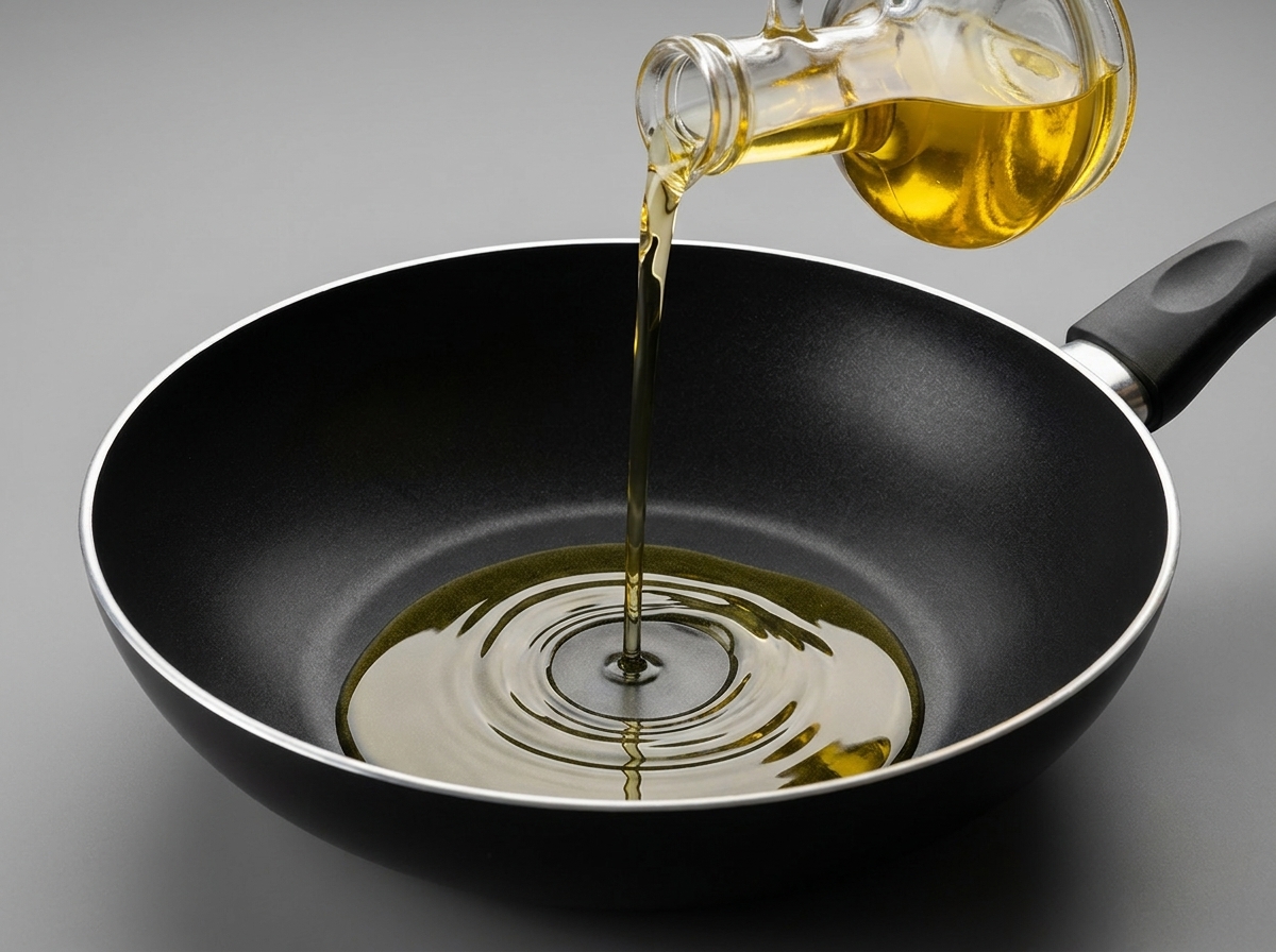 Aceite de cocina transparente vertiéndose desde una botella de vidrio en un wok negro antiadherente.