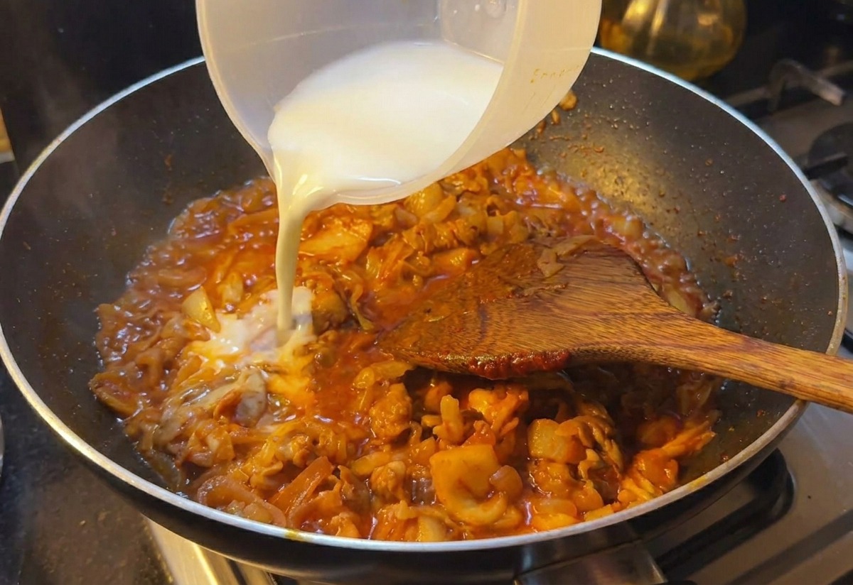 Agua con almidón de color blanquecino vertiéndose en una sartén con ternera y kimchi en salsa roja.